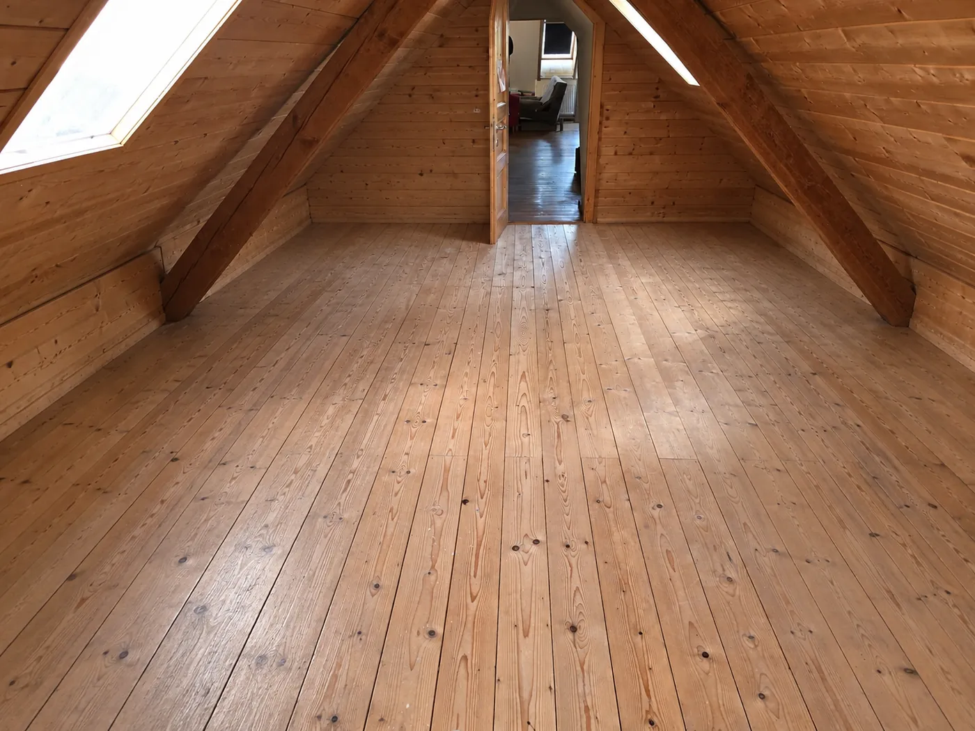 Dachbodenräumung Mistelbach: vollständig geräumter Dachboden mit freiem Holzboden, Dachbalken und zwei Dachfenstern
