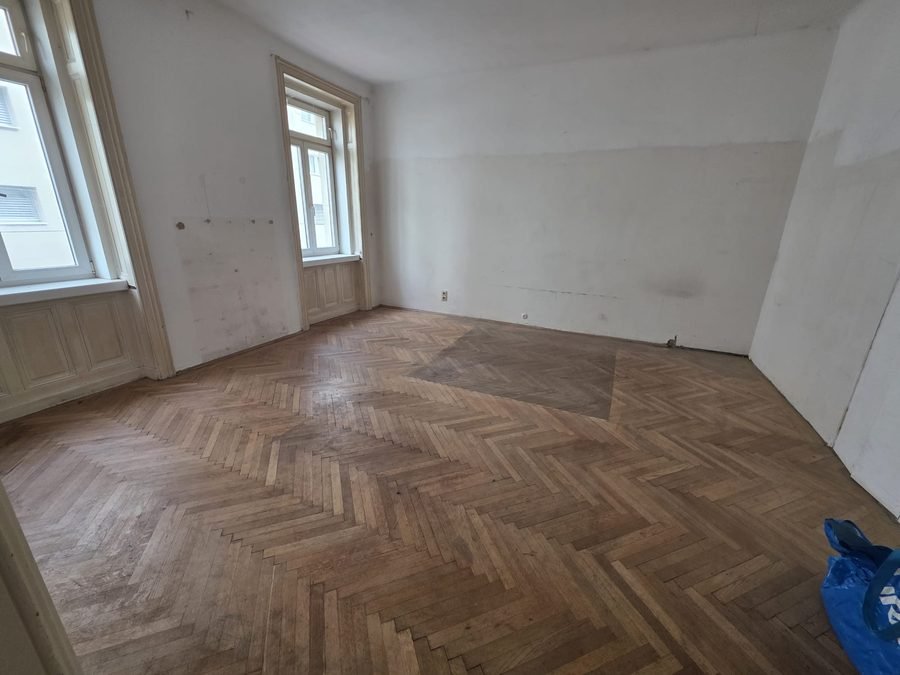 Verlassenschaft Entrümpelung Wien 1010 Innere Stadt: leeres Zimmer nach der Räumung mit sichtbarem Parkettboden und zwei hohen Fenstern